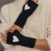 Black fingerless gloves with white heart designs worn by a person in a beige sweater.