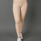 A model wearing a matching beige activewear set consisting of a sports bra and high-waisted leggings, paired with white sneakers, against a solid gray studio background.