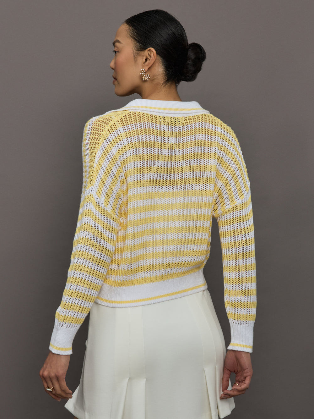 Model wears a lightweight collared open knit yellow and white striped sweater. 