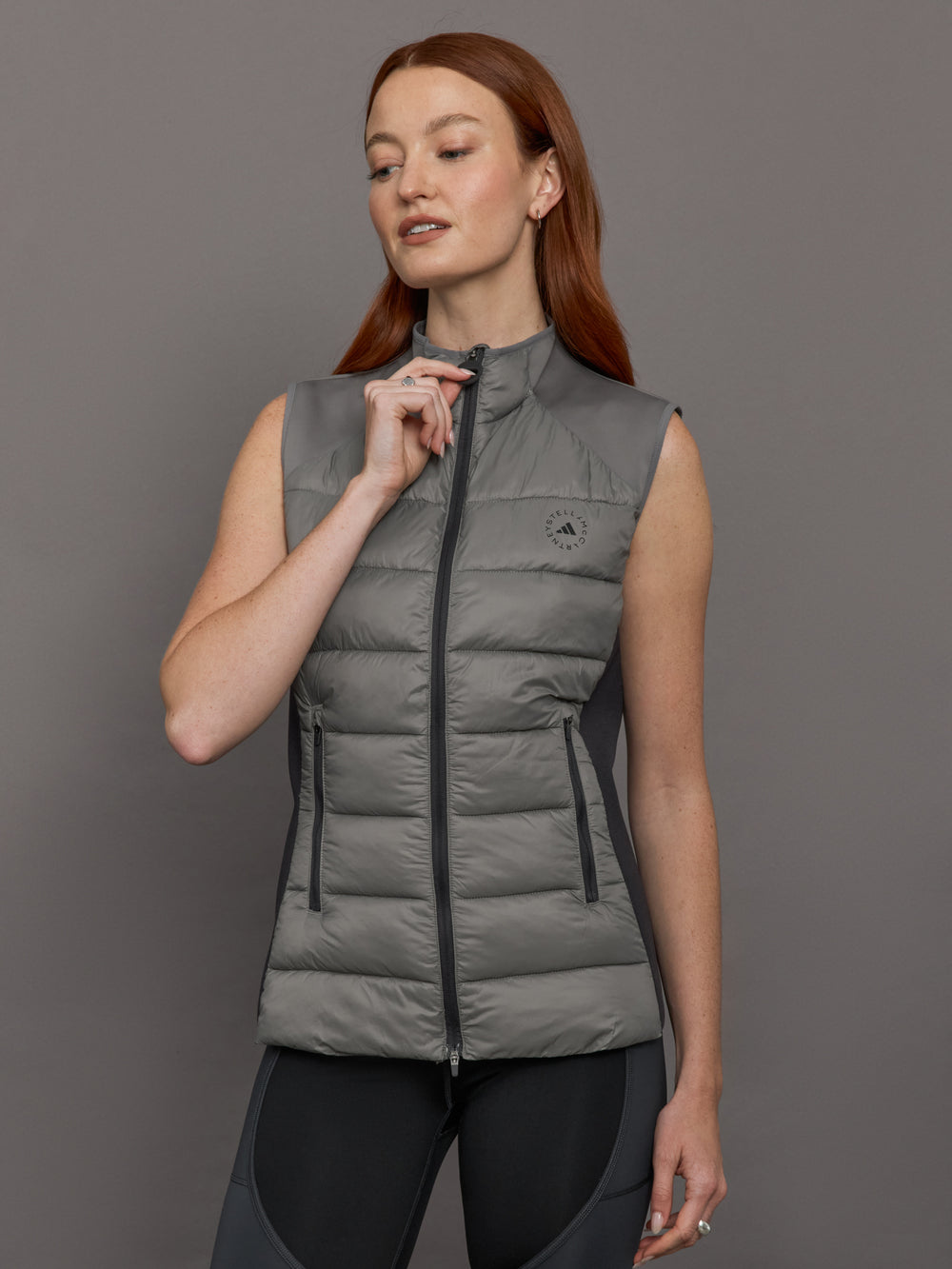 Model wears sleeveless grey golf vest with a high collar, front zipper, and side zip pockets.





