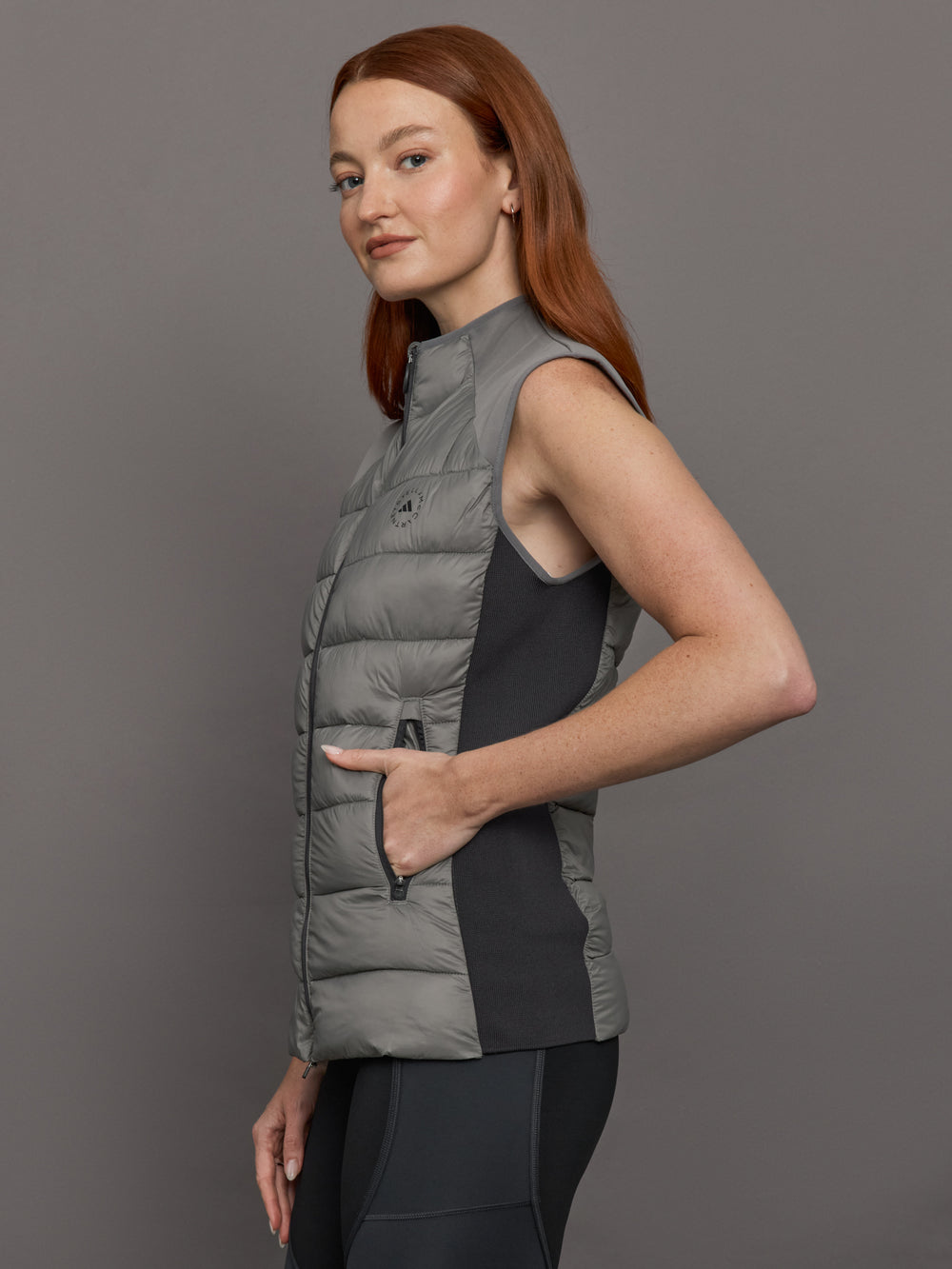 Model wears sleeveless grey golf vest with a high collar, front zipper, and side zip pockets.
