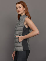 Model wears sleeveless grey golf vest with a high collar, front zipper, and side zip pockets.
