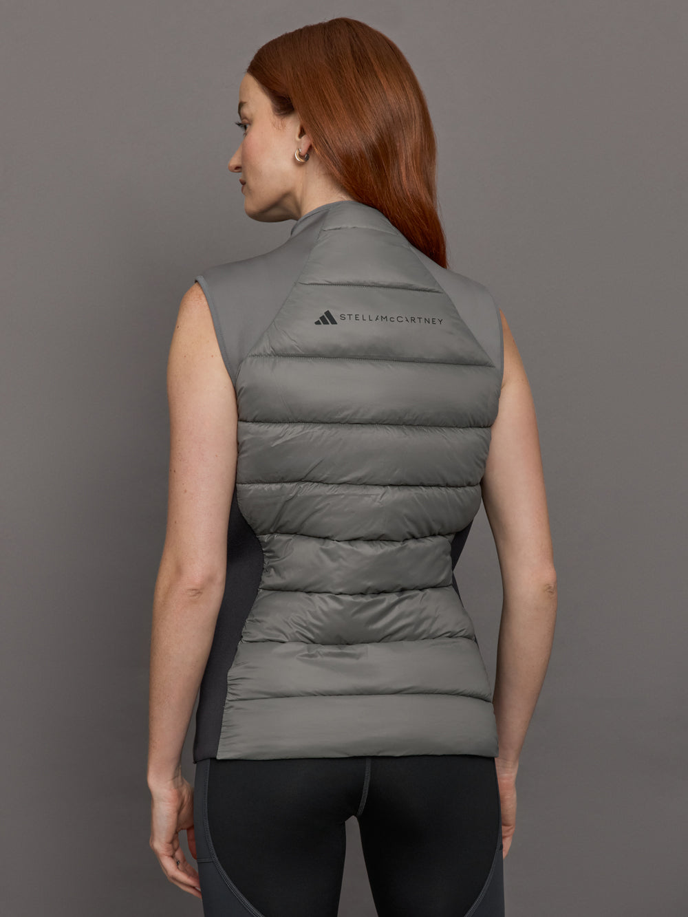 Model wears sleeveless grey golf vest with a high collar, front zipper, and side zip pockets.
