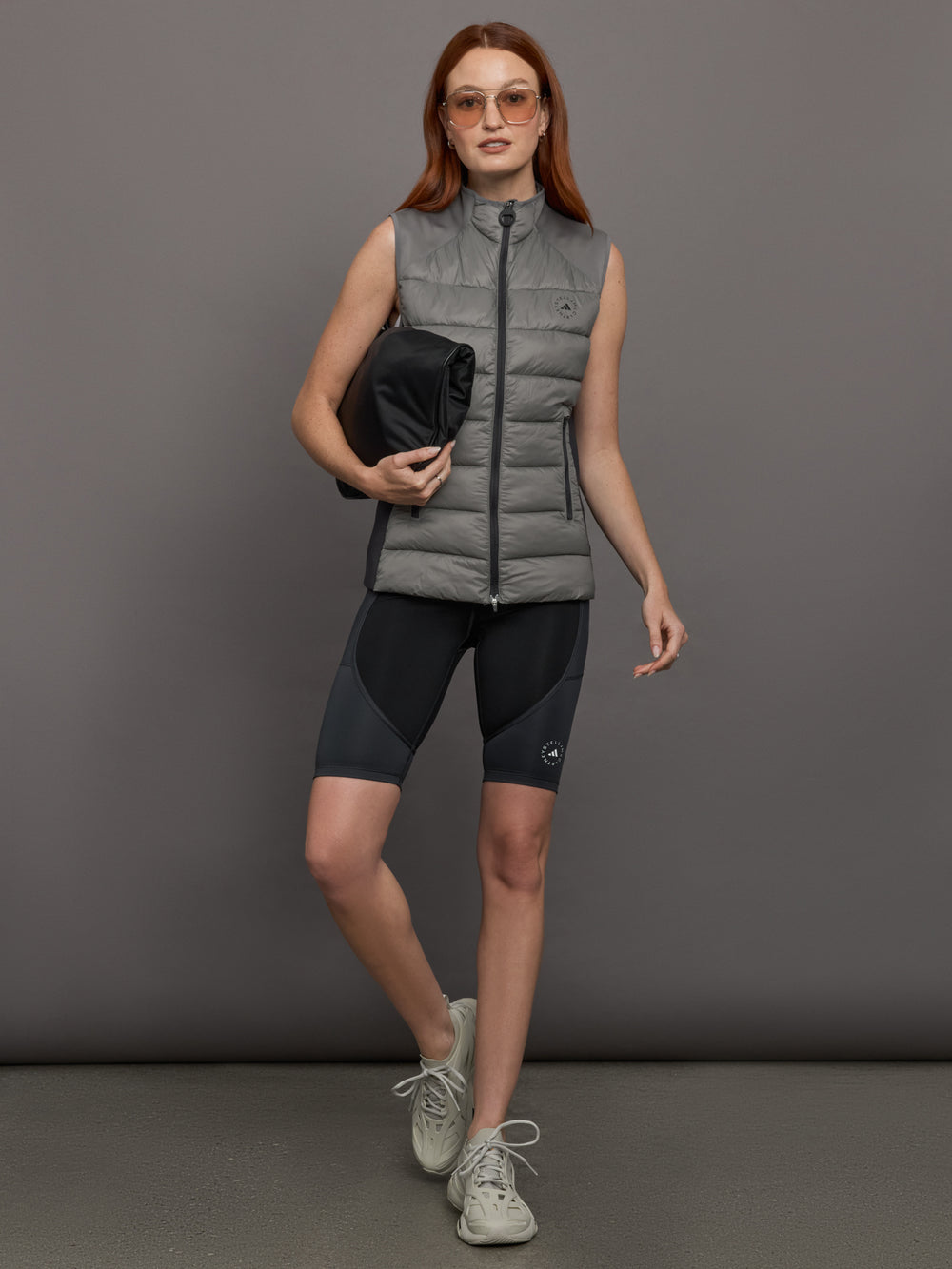 Model wears sleeveless grey golf vest with a high collar, front zipper, and side zip pockets.
