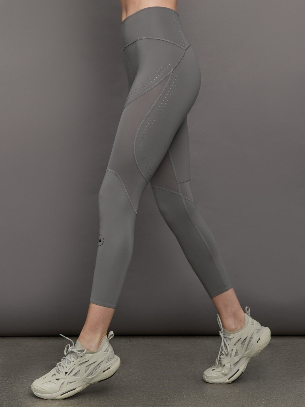 Model wears high-rise grey leggings with a wide elastic waistband, laser-cut perforations, and a small back pocket.
