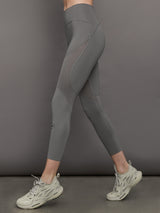 Model wears high-rise grey leggings with a wide elastic waistband, laser-cut perforations, and a small back pocket.
