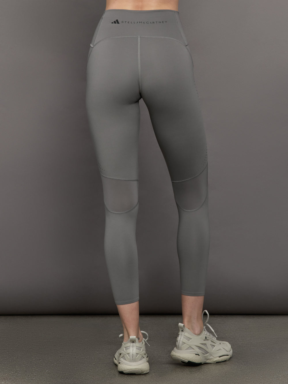 Model wears high-rise grey leggings with a wide elastic waistband, laser-cut perforations, and a small back pocket.
