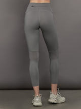Model wears high-rise grey leggings with a wide elastic waistband, laser-cut perforations, and a small back pocket.
