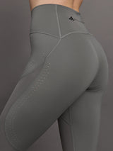 Model wears high-rise grey leggings with a wide elastic waistband, laser-cut perforations, and a small back pocket.
