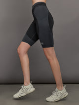 Model wears black and dark grey two-tone biker shorts with a high-rise waistband and an open side pocket.
