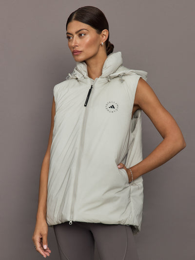 Woman wearing a light gray puffer vest with a brand logo on a plain background