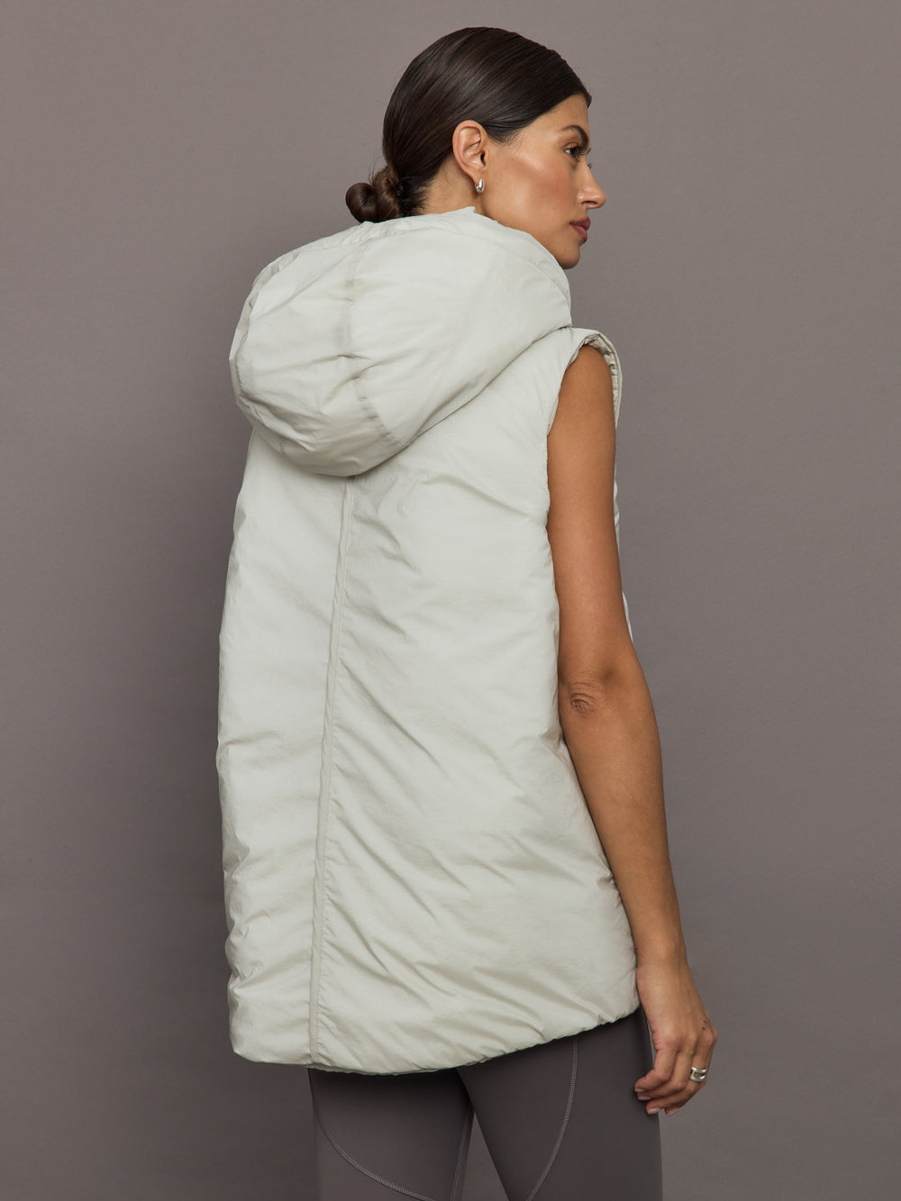 Woman wearing a light gray puffer vest against a plain background
