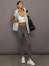 Woman in athletic wear holding a black bag against a gray background