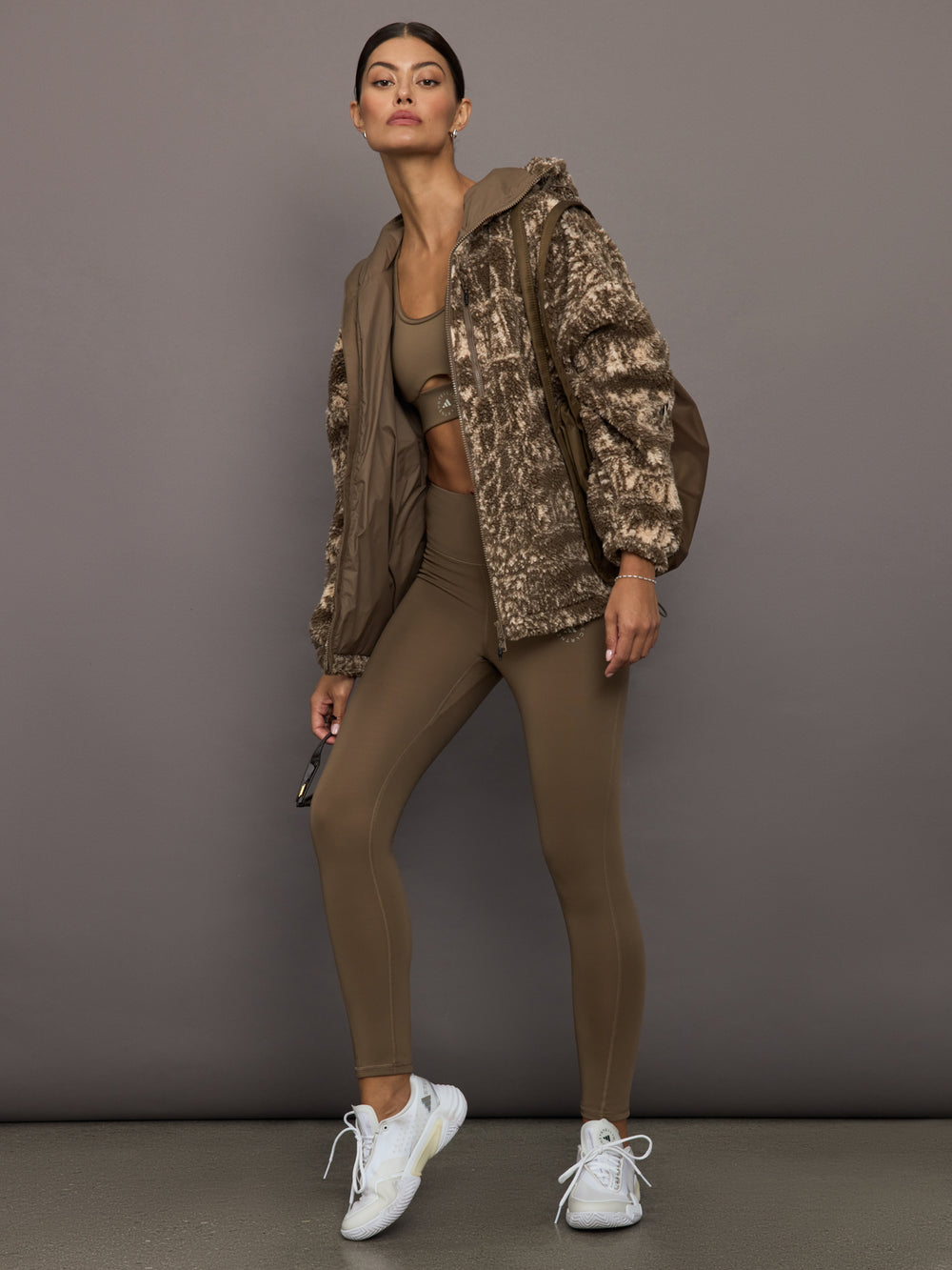 Woman wearing a camouflage jacket and brown outfit against a gray background