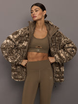 Woman wearing a camouflage jacket over athletic wear on a gray background