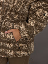 Close-up of a person wearing a brown and beige patterned jacket with a neutral background