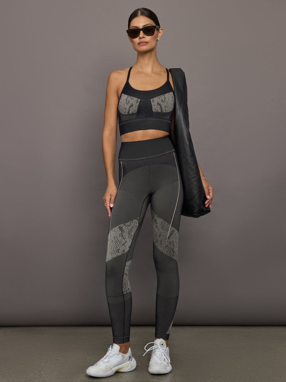 Woman wearing a black sports bra and leggings with snakeskin details, standing against a gray background.