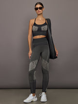 Woman wearing a black sports bra and leggings with snakeskin details, standing against a gray background.