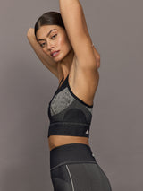Woman wearing a black sports bra with Adidas logo on a gray background