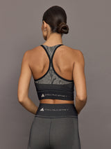 Person wearing a black sports bra and leggings with Adidas branding on a gray background