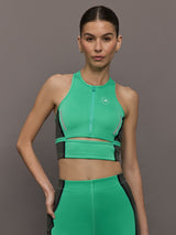 Model wears a bright green cropped sleeveless activewear tank with gray side paneling and an open horizontal slit below the chest. 