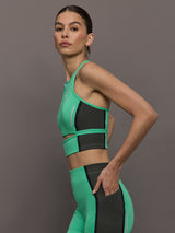 Model wears a bright green cropped sleeveless activewear tank with gray side paneling and an open horizontal slit below the chest. 
