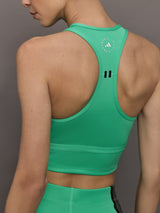 Model wears a bright green cropped sleeveless activewear tank with gray side paneling and an open horizontal slit below the chest. 