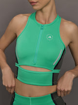 Model wears a bright green cropped sleeveless activewear tank with gray side paneling and an open horizontal slit below the chest. 