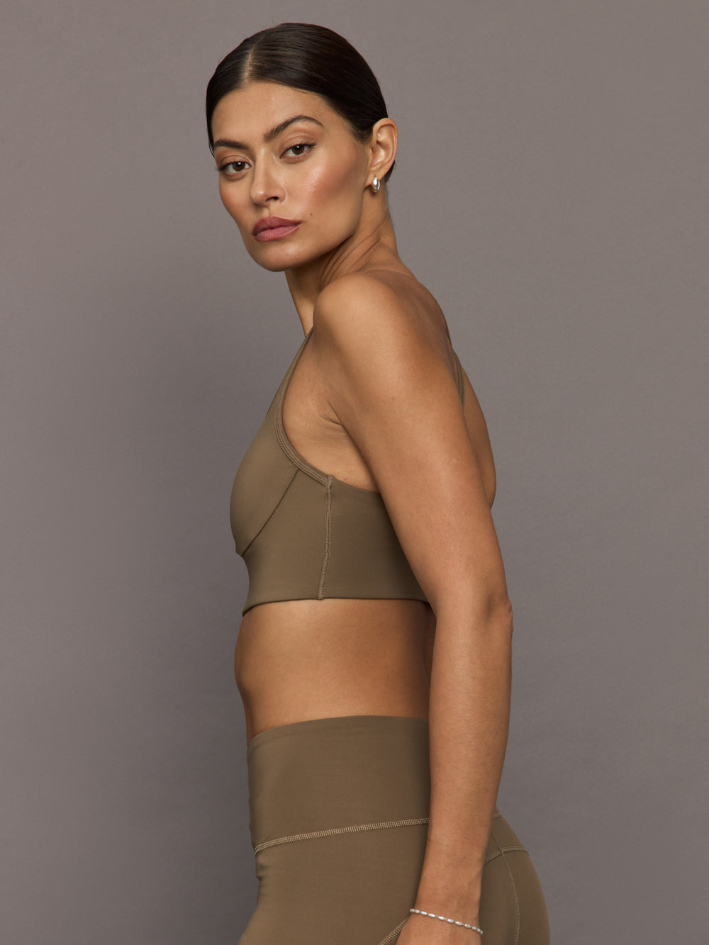 Woman wearing a brown sports bra and leggings against a gray background