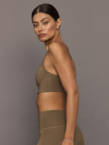 Woman wearing a brown sports bra and leggings against a gray background
