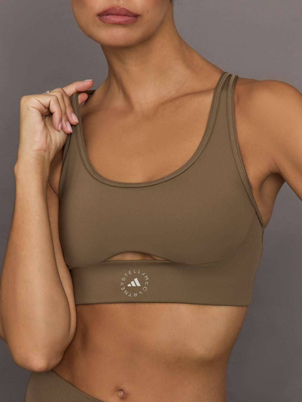 Woman wearing a brown sports bra with Adidas logo on a neutral background