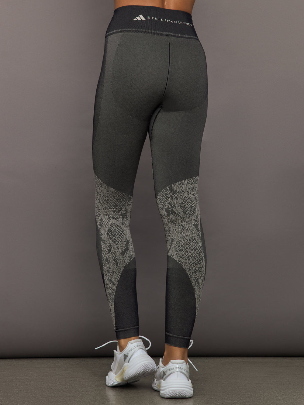 Person wearing dark gray leggings with snake print pattern on a gray background
