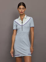 Woman wearing a light blue dress with white collar and purple accents against a gray background