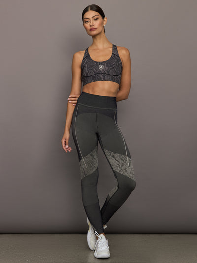 Model wears black/charcoal Adidas sports bra with logo in the center.