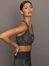 Model wears black/charcoal Adidas sports bra with logo in the center.