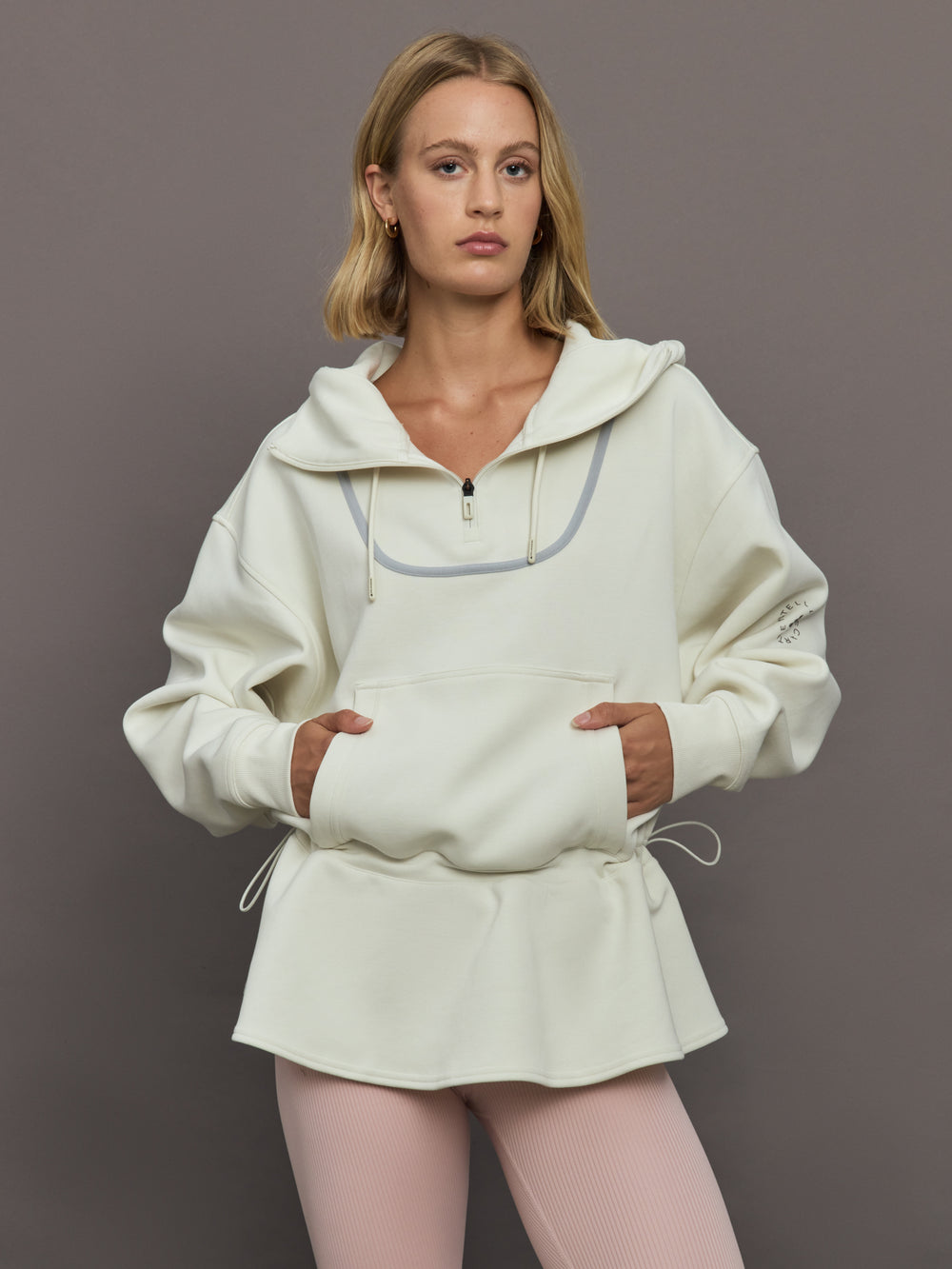 Model wearing a cream-colored hoodie with a quarter zip.