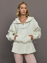 Model wearing a cream-colored hoodie with a quarter zip.