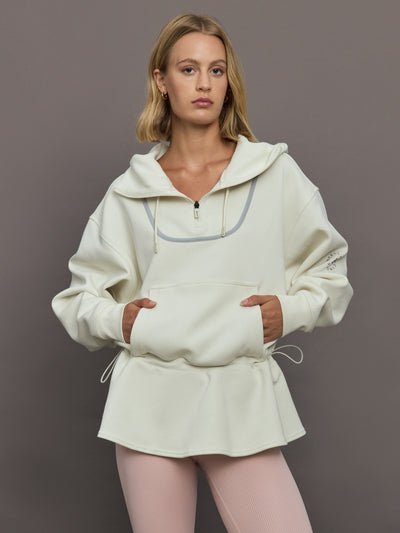 Model wearing a cream-colored hoodie with a quarter zip.