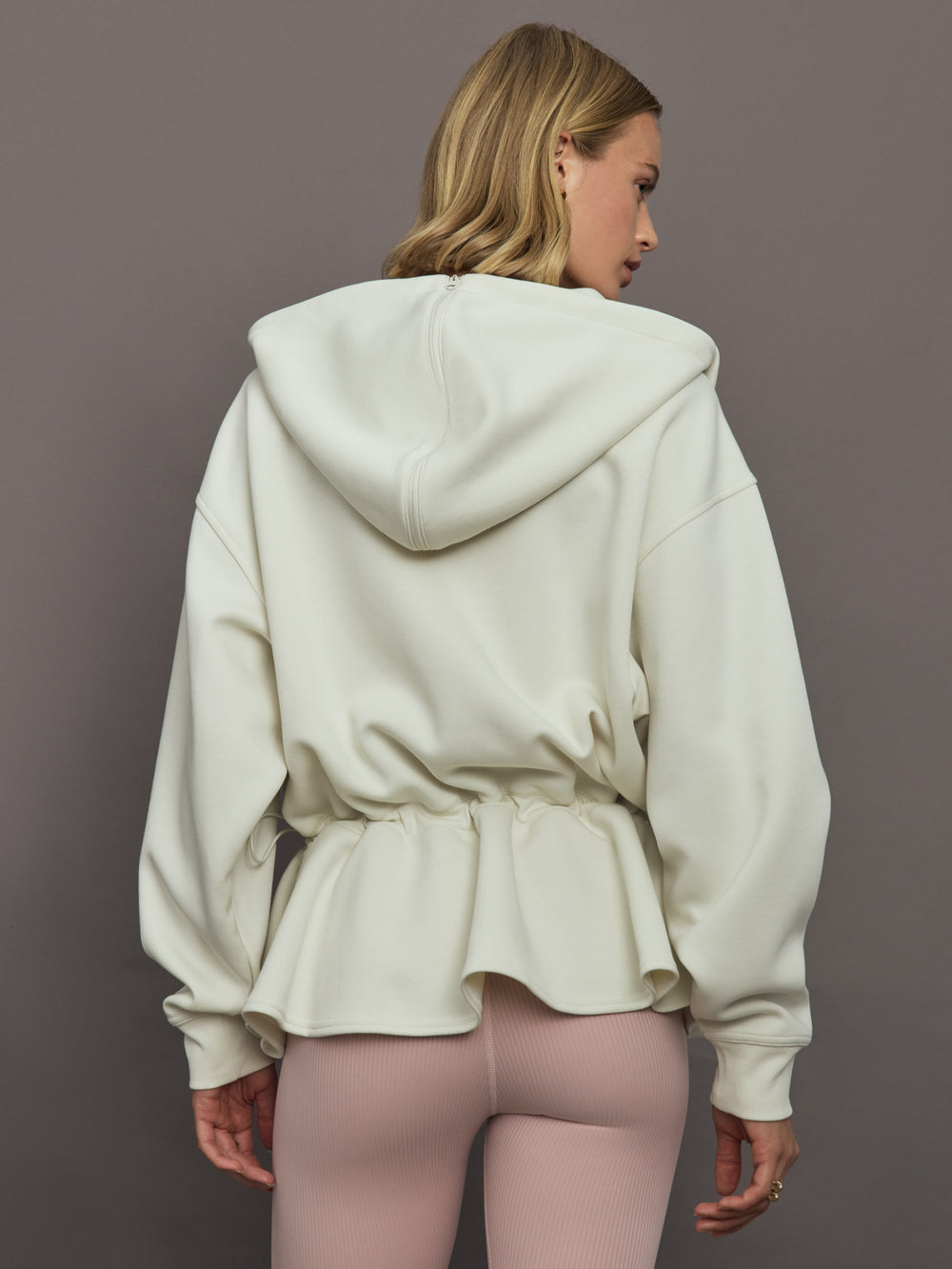 Model wearing a cream-colored hoodie with a quarter zip.