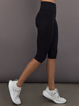 Model is wearing Yoga Interlock High-Waisted Capri Legging in Black, side profile view.