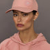 Person wearing a pink Adidas cap and hoodie against a gray background