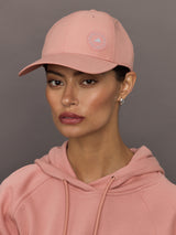 Person wearing a pink Adidas cap and hoodie against a gray background