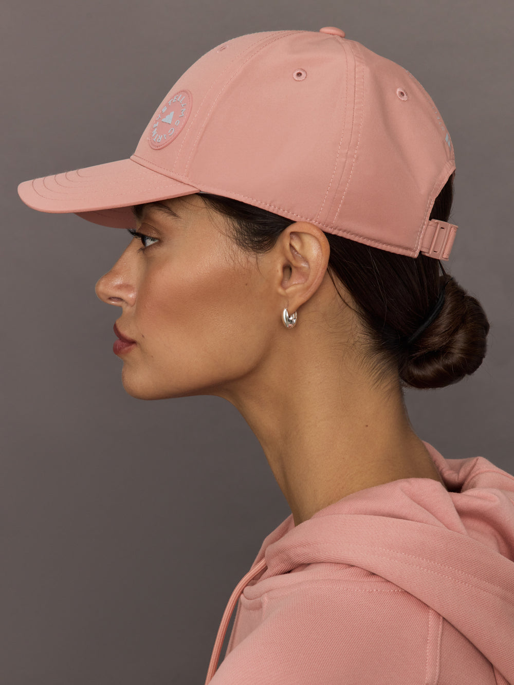 Woman wearing a pink cap and matching hoodie against a gray background