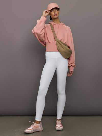 Person wearing a pink hoodie, white leggings, and pink sneakers against a gray background