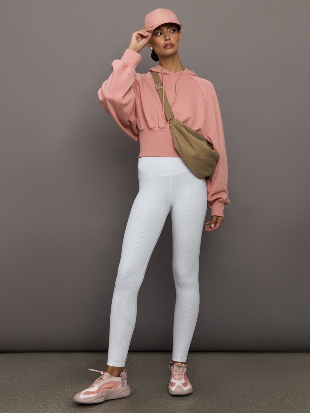 Person wearing a pink hoodie, white leggings, and pink sneakers against a gray background