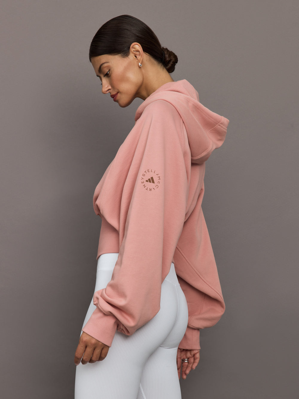 Woman wearing a pink hoodie with a logo on a gray background