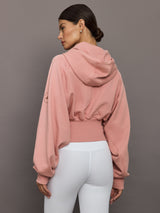 Person wearing a pink hoodie and white pants against a gray background