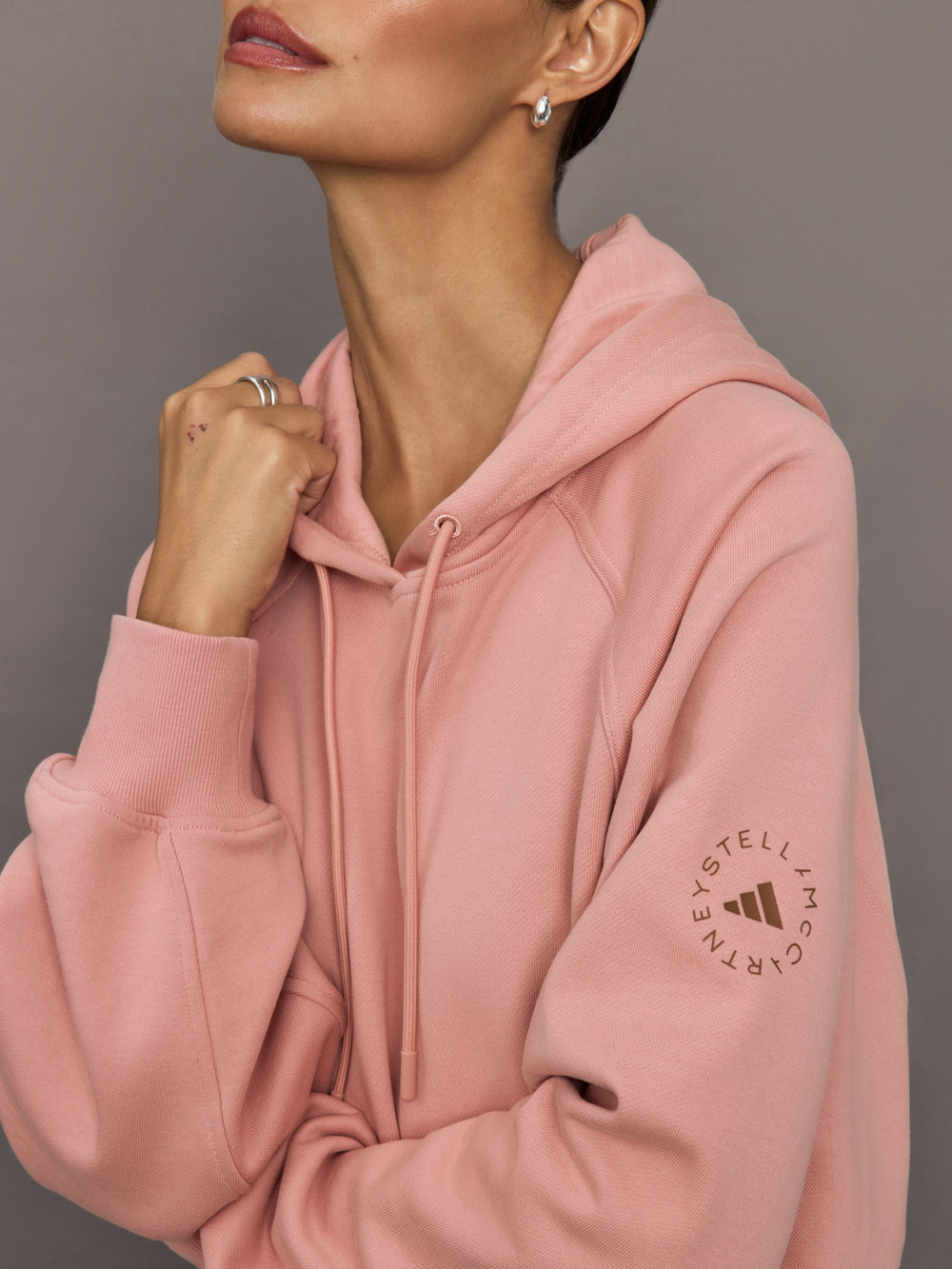 Pink hoodie with a brand logo on the sleeve against a neutral background