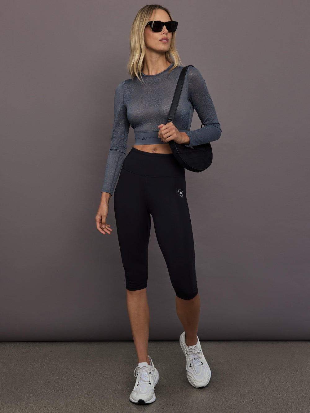 Model is wearing Yoga Interlock High-Waisted Capri Legging in Black, full body walking view.
