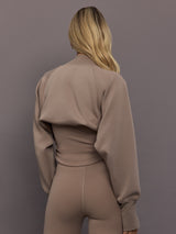 Model is wearing Studio Double Knit Cropped Shrug in Chalky Brown, back view.